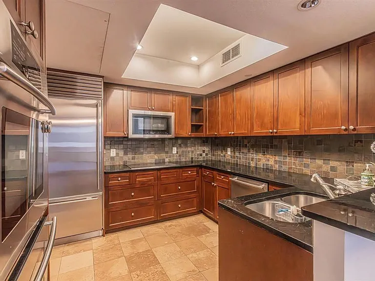 Gourmet kitchen featuring stainless steel appliances, dark wood cabinetry, a tiled backsplash, granite countertops, and light-toned tile flooring