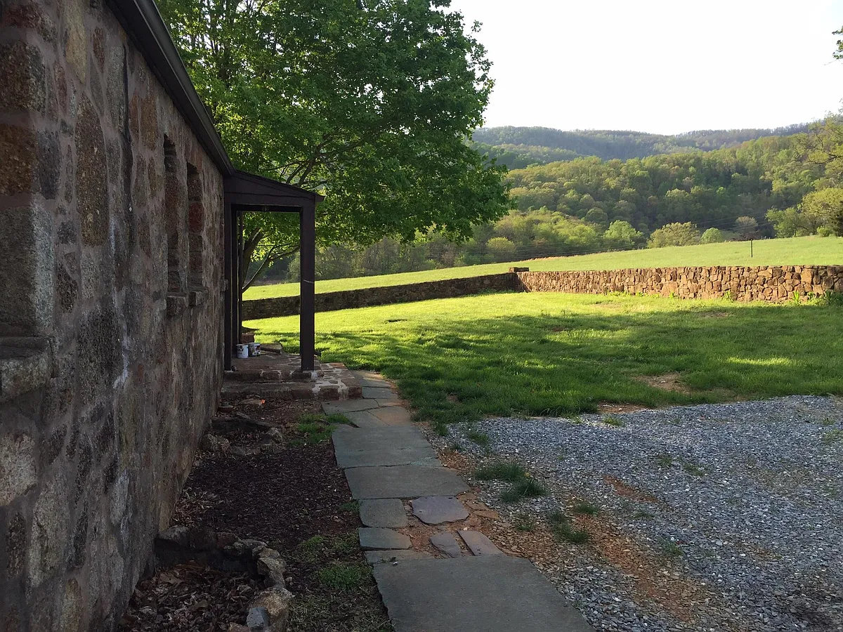 Side entrance with gravel parking pad and a view out west. The yard is enclosed with a beautiful stone wall and has a large mature tree. - 397 Fairlea Ln