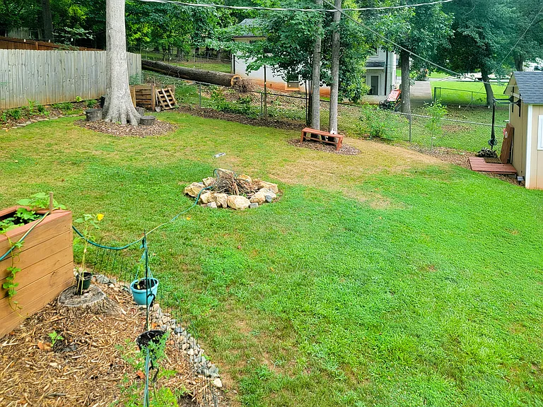 Summer photo of the yard, showcasing a secondary garden area, the fire pit, mature trees, and flowerbeds. 
An ideal space for dogs to run and play!