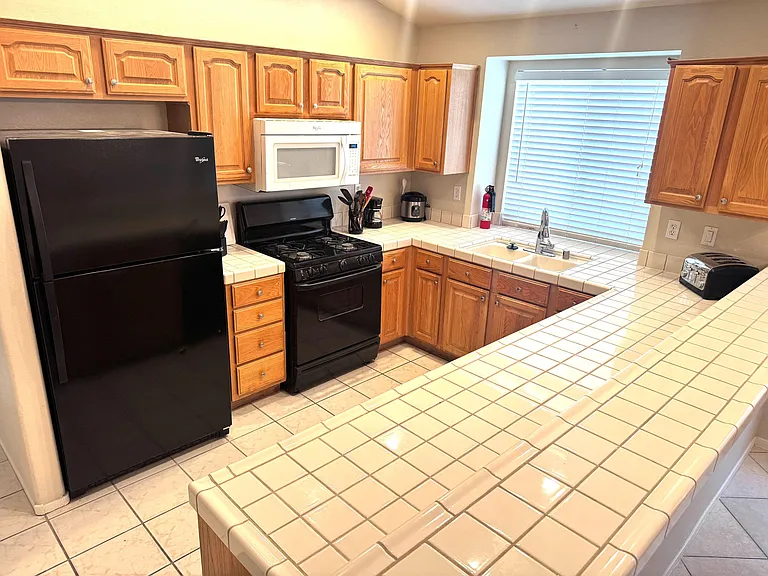 Functional U-shaped kitchen with generous tile counters, ample wood cabinetry, and a full appliance set plus windowed sink.
