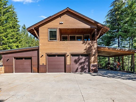 View of the front of large home with 3 car garage and huge carport. Check out the concrete retaining wall on the left. It is built to resemble mountain tree trunks. The architecture in this home is incredible.