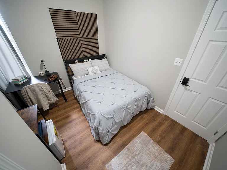Furnished bedroom with a full-size bed, work desk, and window with curtains, plus durable wood-look flooring.