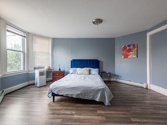 Spacious bedroom with large bay windows, hardwood-style flooring, and room for a full/queen bed plus side tables.