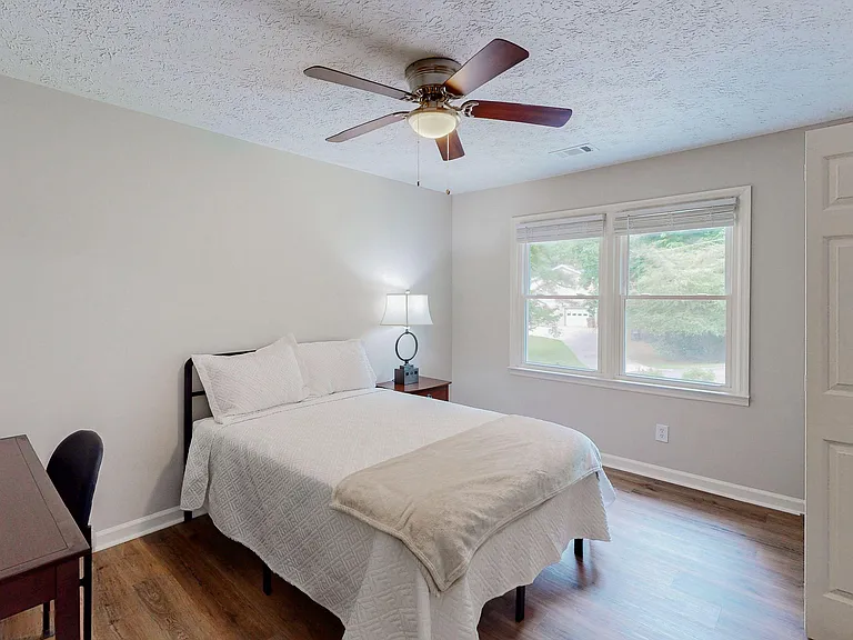 Private bedroom with a ceiling fan, wood-look flooring, and a large window for natural light and outdoor views.