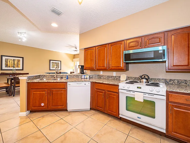 Open kitchen with ample wood cabinetry, granite-look counters, and full appliance set, flowing into a dining area.