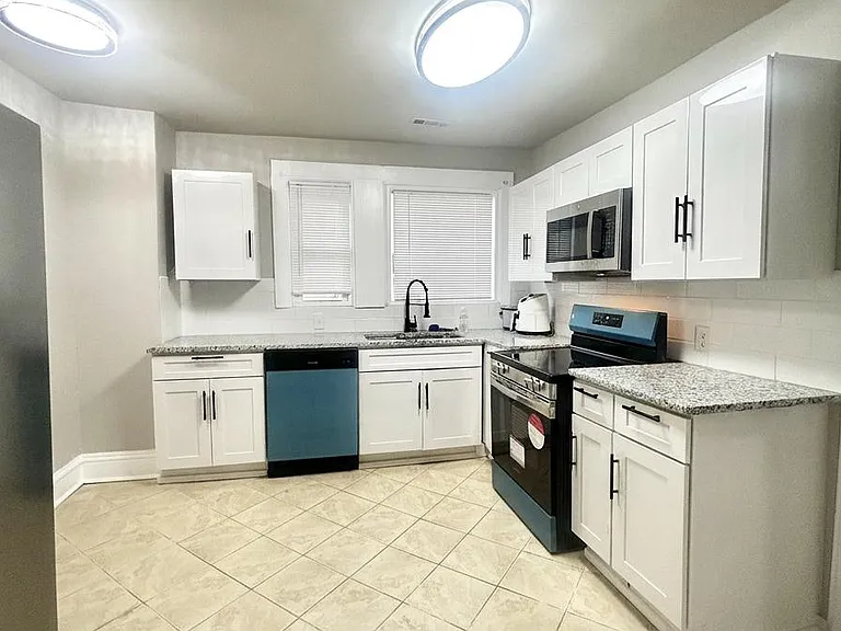 Spacious kitchen with ample white cabinetry, granite-look counters, and stainless appliances plus a windowed sink area.