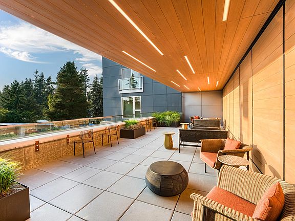 Relax beneath warm wood accents on Modera Shoreline's terrace, offering inviting seating and tranquil treetop views.