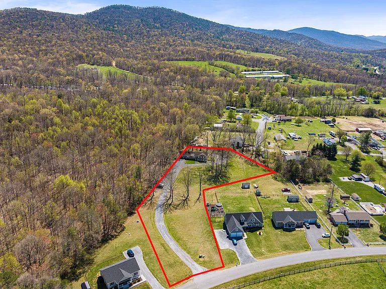 Aerial View showing driveway entrance, paved parking at the tree line and house at the top of hill.