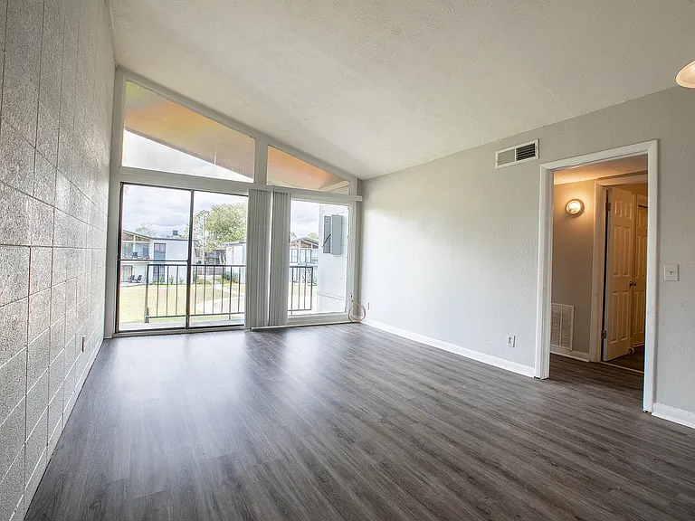Bright, open living space featuring large windows, vaulted ceiling, and sleek wood flooring, offering a seamless flow to outdoor views.
