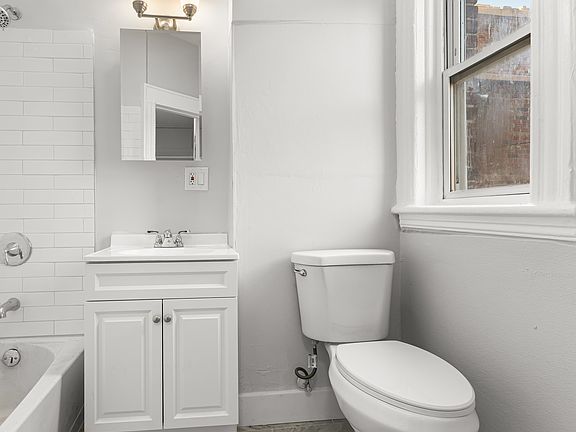 Bright and well_maintained full bathroom featuring classic tile flooring and tiled tub surround. The space includes a full_size bathtub with shower, a modern vanity with sink and cabinet storage, and a wall_mounted mirror with overhead lighting.