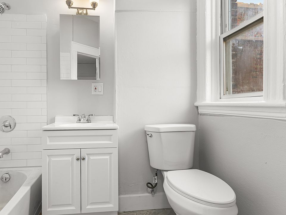 Bright and well_maintained full bathroom featuring classic tile flooring and tiled tub surround. The space includes a full_size bathtub with shower, a modern vanity with sink and cabinet storage, and a wall_mounted mirror with overhead lighting.