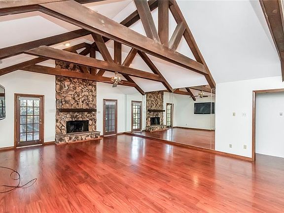 Unfurnished living room featuring ceiling fan, wood-type flooring, a fireplace, and beamed ceiling