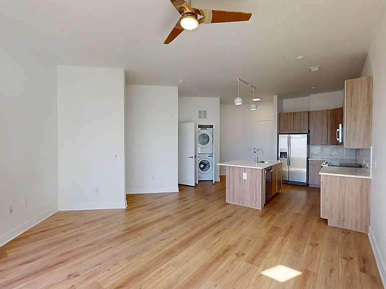 Apartment kitchen with stainless steel appliances, dining and living room with wood-style flooring.