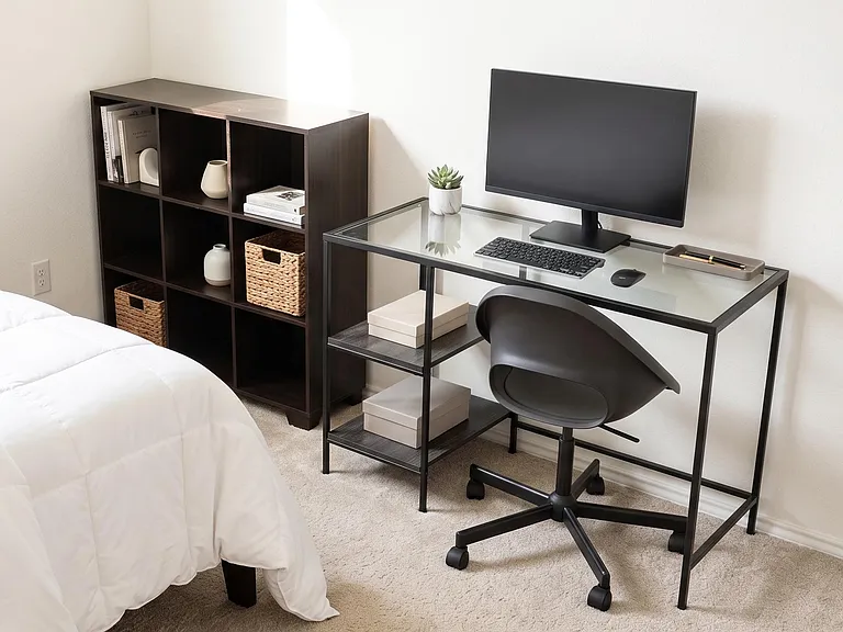 Furnished bedroom corner with a dedicated desk setup, storage cubbies, and carpeted floors for comfortable daily living.