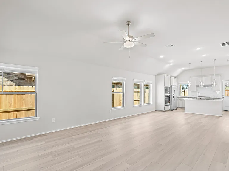 Expansive open-concept family room with vaulted ceiling, ceiling fan, luxury vinyl plank floors, and seamless flow into the kitchen and dining area.