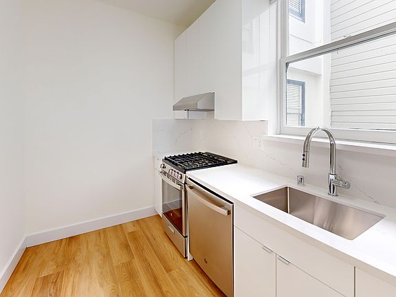 Kitchen featuring stainless steel appliances, sleek cabinets, a marble countertop, and a large window for natural light