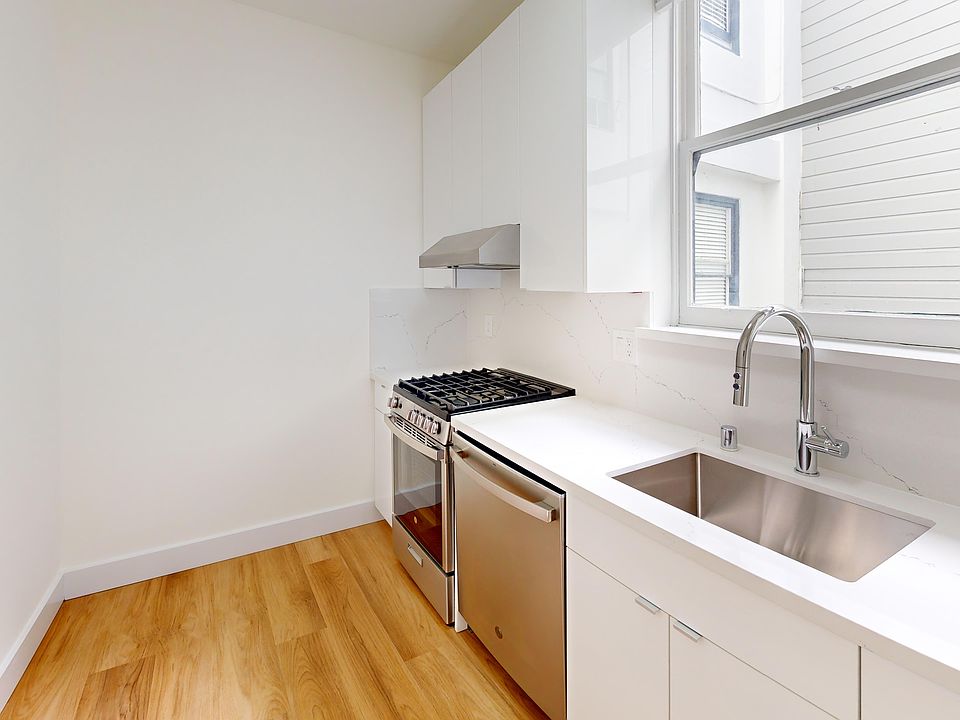 Kitchen featuring stainless steel appliances, sleek cabinets, a marble countertop, and a large window for natural light