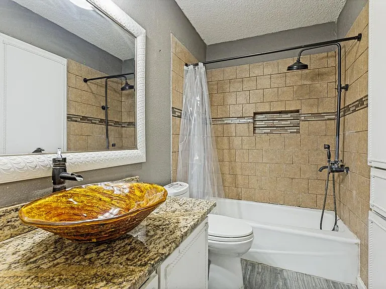 Full bath with tiled tub/shower, granite-topped vanity with vessel sink, and wall mirror for daily convenience.
