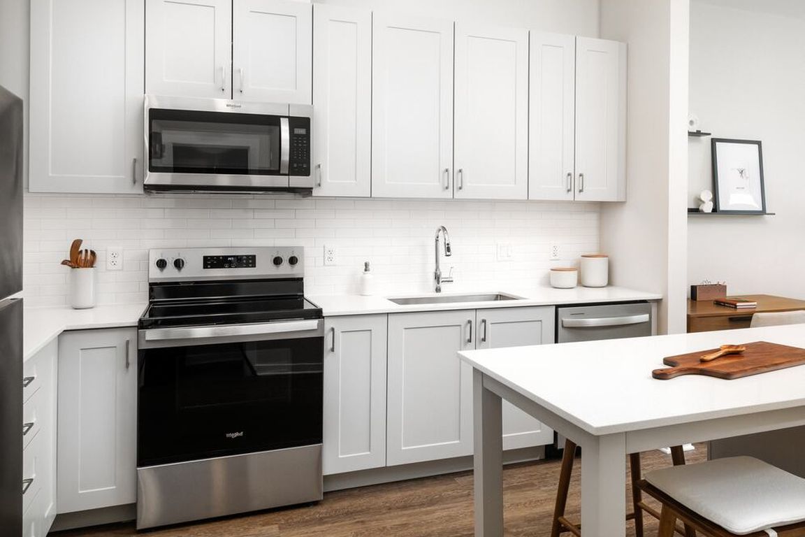 New West Phase - Finish Package III Kitchen with stainless steel appliances, white quartz countertops, grey cabinetry, pendant lighting, and hard surface flooring
