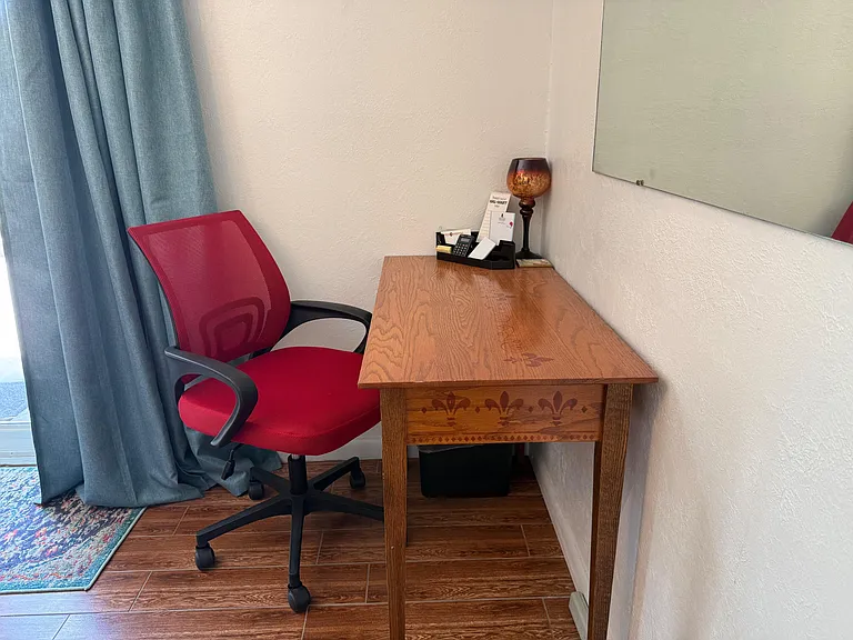Dedicated work nook with a full-size desk, rolling chair, and task lighting, set beside window curtains for daytime use.