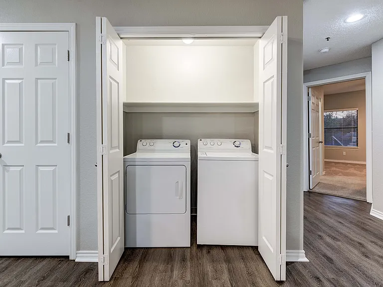 Modern apartment laundry nook with sleek washer and dryer, accented by elegant white bi-fold doors and stylish wood flooring.