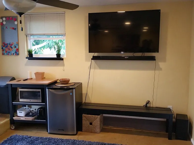 The area under the TV has been converted into a kitchenette with wall shelves. The TV has been moved to an adjacent wall.