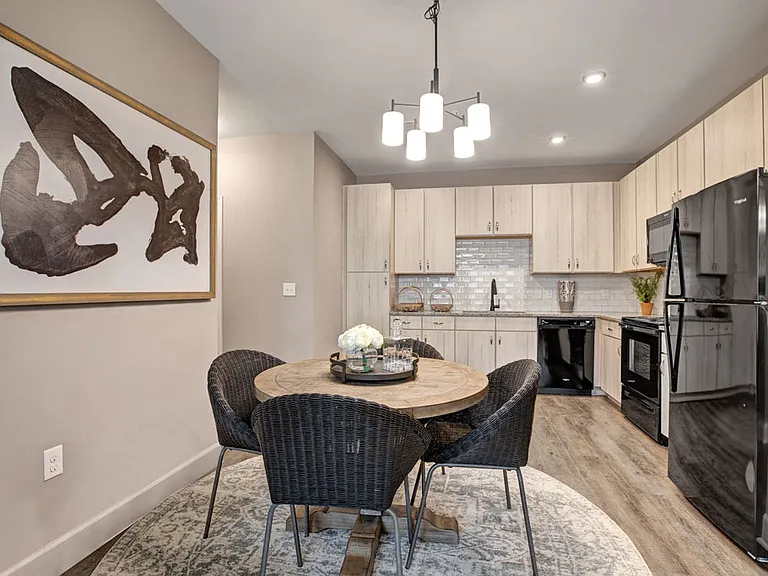 Light ceiling-reaching cabinetry, wood-like plank flooring, sleek black appliances, and white subway tile backsplash