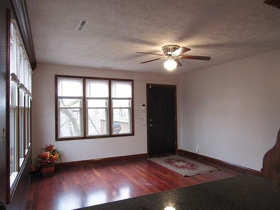 Living room has hardwood floors, built-in writing desk, 3 light colored walls with one accent wall. Brown entry door. Ceiling fan.