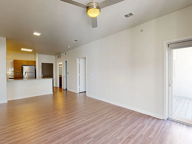 Apartment kitchen with stainless steel appliances, dining and living room with wood-style flooring.