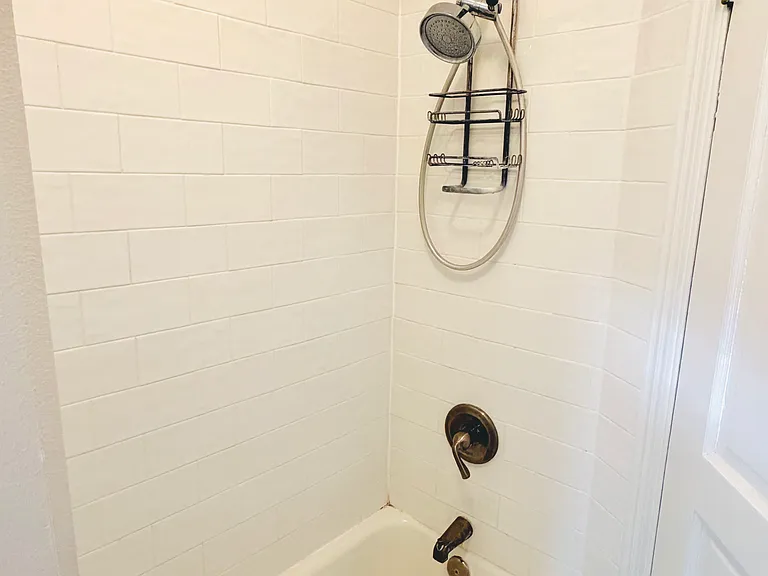 Full bathroom with marble hex tile floor, white beadboard wainscoting, pedestal sink, toilet, and tub/shower combination.