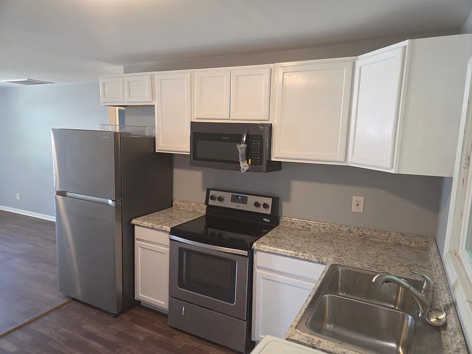 This bright and functional kitchen features modern white cabinetry, granite-look countertops, and a full suite of stainless steel appliances. The efficient layout offers ample cabinet storage and workspace, while the neutral color palette creates a clean,