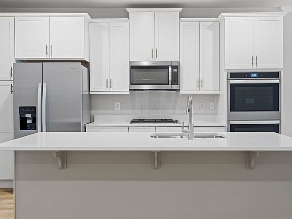 Spacious kitchen to Upper and lower white cabinets, light toned wood floors, stainless appliances, a