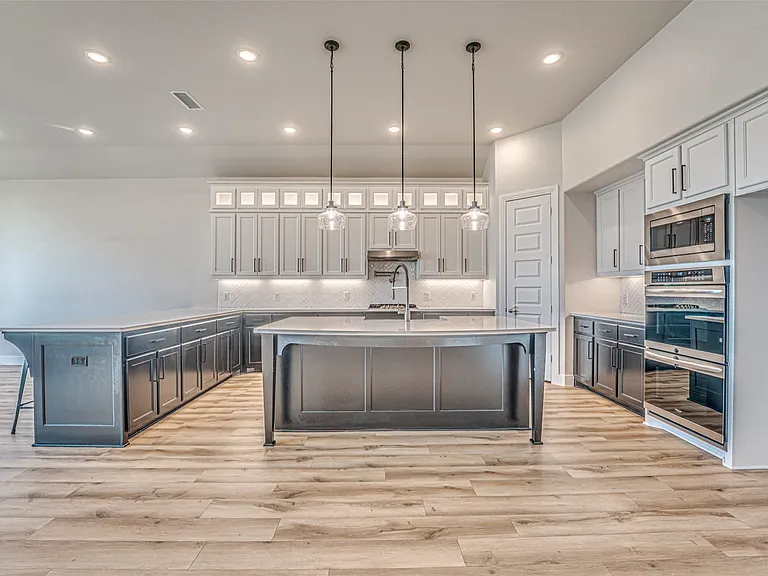 Spacious kitchen featuring an extended island, wood-finish flooring, recessed lighting, pendant lighting, and stainless steel appliances