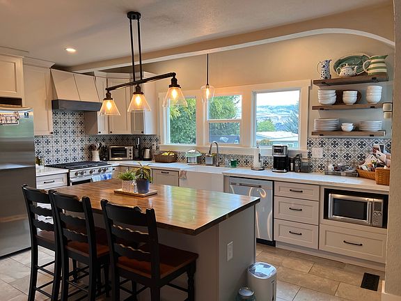 Large kitchen with stainless steel appliances, open shelves, quartz counters and butcher block island with seating for 3.