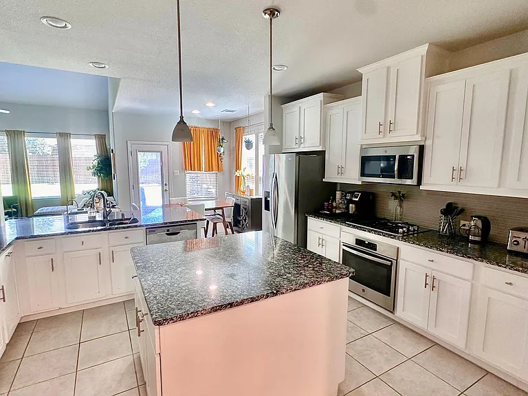 Open kitchen with large granite island, ample white cabinetry, and stainless appliances, flowing into the dining area.