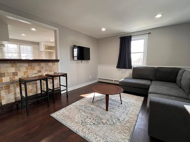 Comfortable living room with sectional seating, wall-mounted TV, and a breakfast bar opening to the kitchen.