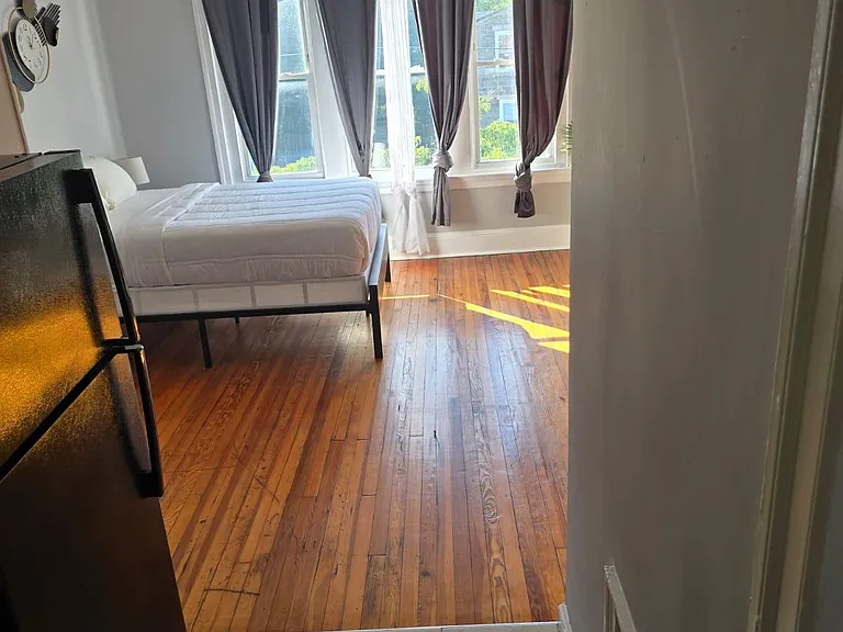 Furnished bedroom with hardwood floors, a full-size bed, and large windows with curtains for privacy and natural light.