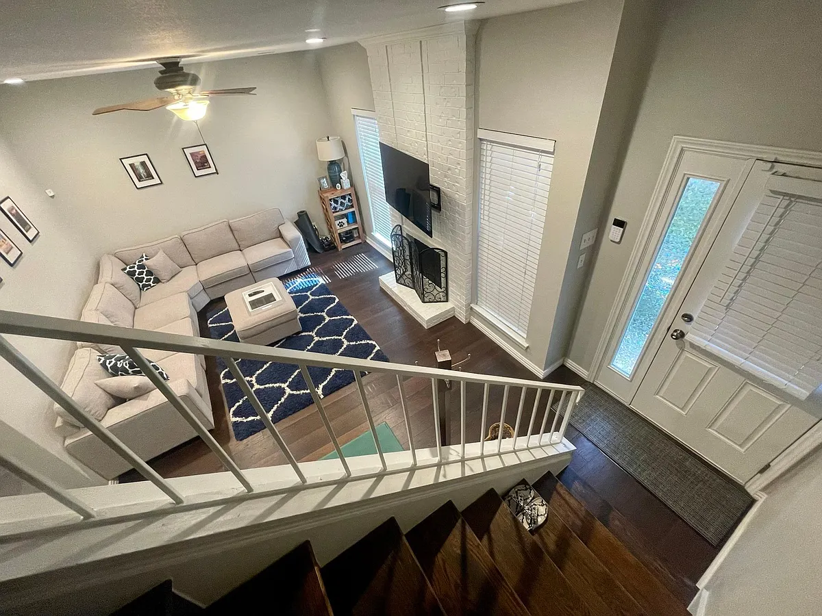 View from the stairs to the living room with wood burning fireplace and windows to the courtyard! A closet is located under the stairs for additional storage space. - 5740 Richmond Ave #104