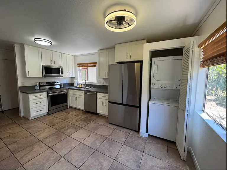 Kitchen photo facing south. Washer and dryer in unit. Over is also an air fryer. Window above the sink is facing South. The open window on the right faces West. Refrigerator and Stove are Samsung.