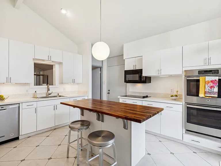 Kitchen featuring white cabinetry, light-toned countertops, and stainless steel appliances, including double wall ovens and a dishwasher