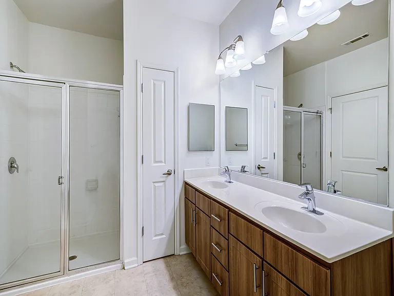 Elegant bathroom with dual sinks, wooden cabinetry, and a spacious glass-enclosed shower.