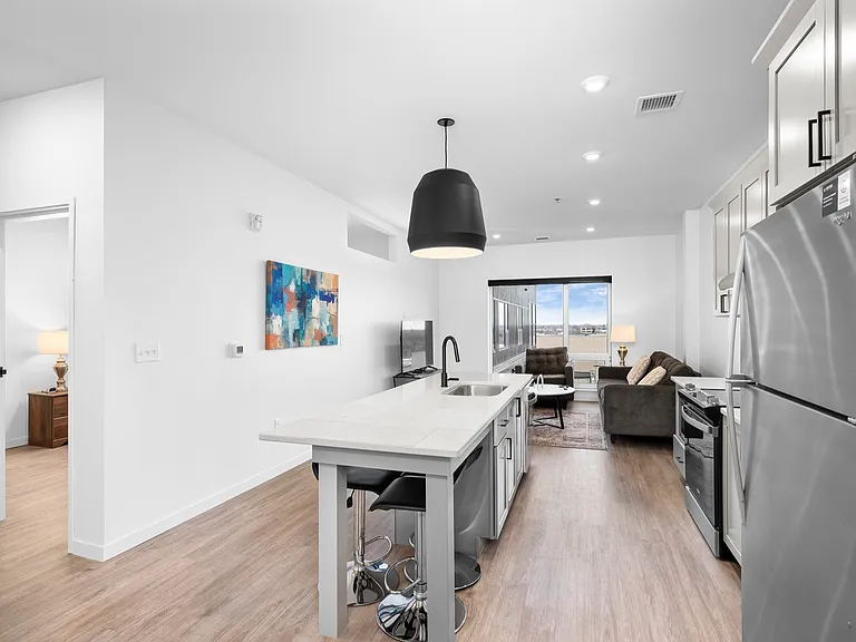 Modern open-concept kitchen and living room with sleek finishes, featuring a cozy sofa, vibrant artwork, and large window with city view. Modern open-concept kitchen and living room with sleek finishes, featuring a cozy sofa, vibrant artwork, and large wi
