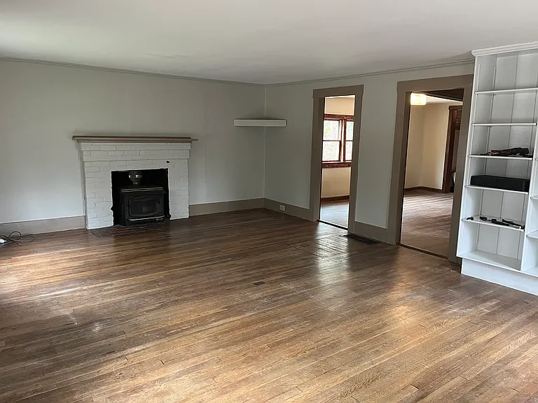 Spacious living room with hardwood floors, floor to ceiling bookcases and decorative fireplace with mantle