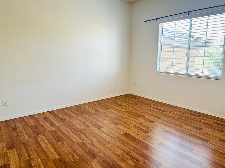North-facing upstairs bedroom overlooking the front yard and street, with natural light and wood-look flooring.