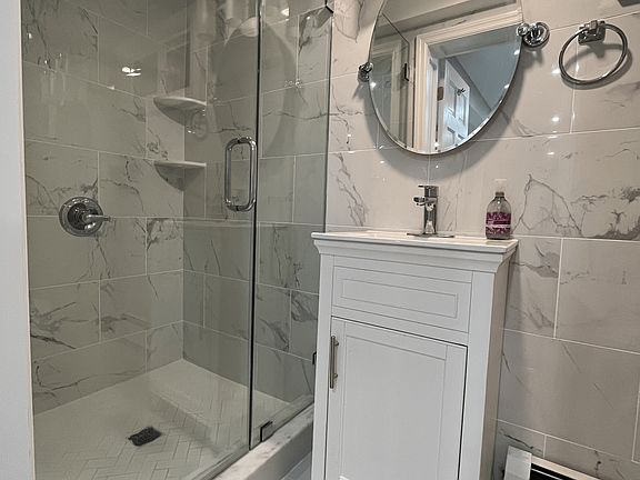 Elegant and modern bathroom featuring a sleek glass-enclosed shower, stylish vanity with ample storage, and luxurious marble-style tile throughout. A perfect blend of sophistication and functionality!
