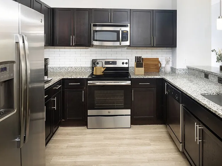 Renovated Package II Kitchen with dark cabinetry, speckled granite countertops, white tile backsplash, stainless steel appliances, pendant lighting, and hard surface flooring