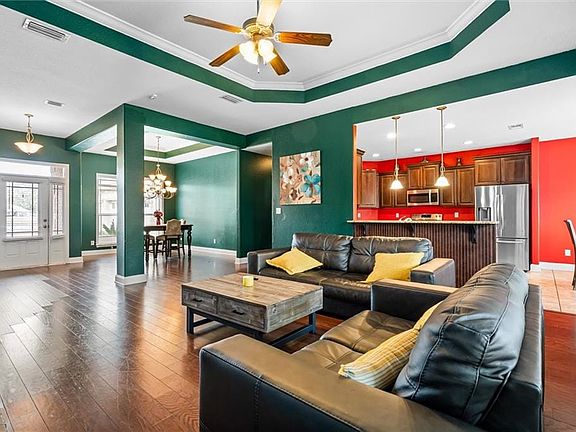 Living room with a tray ceiling, crown molding, dark hardwood / wood-style flooring, and ceiling fan with notable chandelier