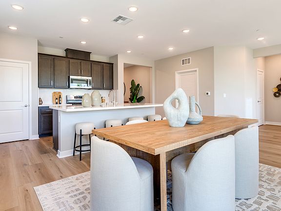 A modern and spacious kitchen and dining area with wooden floors, dark cabinets, a large wooden tabl