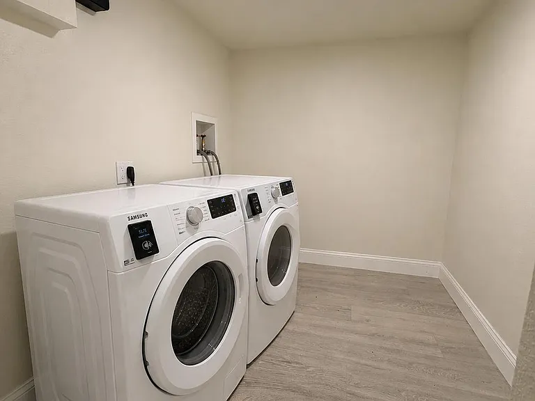 Dedicated laundry room with side-by-side front-load washer and dryer, plus durable flooring and open space to sort clothes.