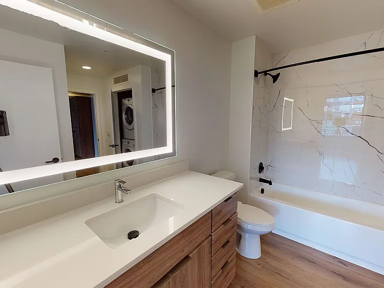 Apartment bathroom with wood-style flooring and LED vanity mirror.